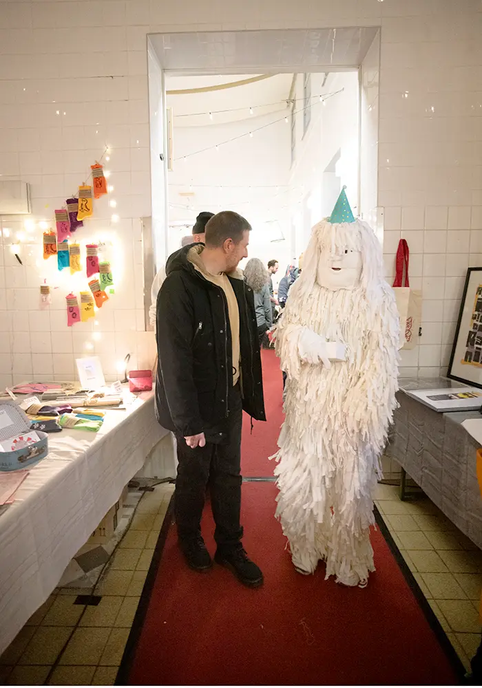 Person in a costume made of white fringes walks through the market.