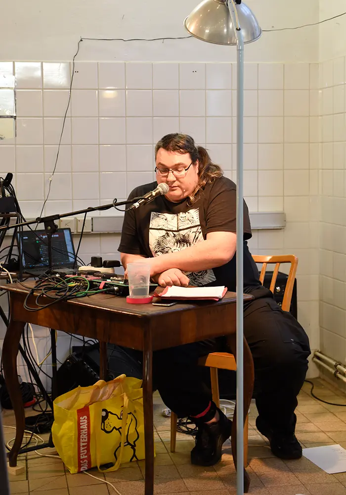Jopa Jotakin sitting infront of a small desk reading a performance